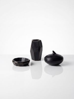 trois vases noirs posés les uns à côté des autres sur une surface blanche