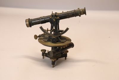 un petit télescope en laiton posé sur un support, sur une surface blanche