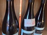 four bottles of wine are lined up on a wooden shelf