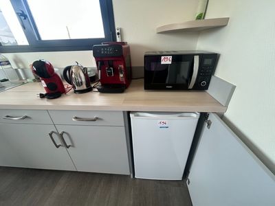 une petite cuisine avec des placards blancs et une cafetière rouge