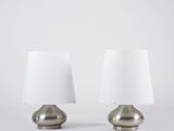 une paire de lampes de table en argent avec des abat-jours blancs sur fond blanc