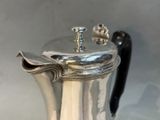 a silver coffee pot on a table with a black handle