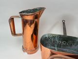 a copper pitcher next to a copper pan on a table