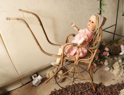 une poupée assise dans une chaise en osier dans un jardin
