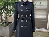 Le manteau est noir et est orné de boutons argentés.