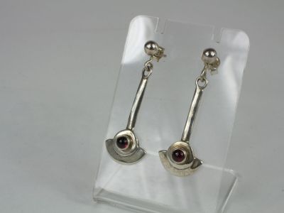 silver earrings with garnets on them on a clear stand