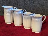 four white pitchers are lined up on a red table cloth