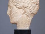 a white marble head of a woman with curly hair on a black stand