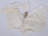 deux robes blanches et un ours en peluche posés sur une surface blanche