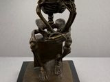 bronze statue of a skeleton with a man sitting on a chair