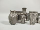 five silver vases sitting next to each other on a white surface