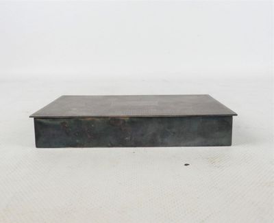 une vieille boîte en métal avec un couvercle, posée sur une surface blanche