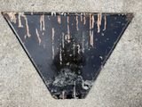 a black triangle with rust on it sitting on the sidewalk