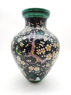 un vase noir avec un couvercle vert sur lequel est représenté un arbre