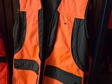 an orange and black vest sitting on top of a shelf next to a red backpack