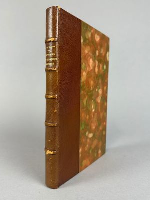 un livre en cuir marron aux tranches dorées posé sur une surface blanche