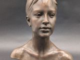 bronze sculpture of a woman ' s head on a gray surface