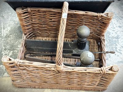 un panier en osier posé par terre, contenant des outils
