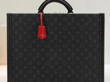 une mallette Louis Vuitton noire avec une poignée rouge, posée sur une table blanche