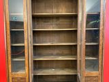 une grande bibliothèque en bois avec des portes vitrées dans une pièce