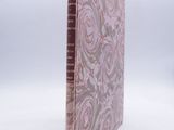 an old book with a pink cover sitting on top of a white surface
