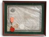 an old document with a red ribbon and a medal in a wooden frame