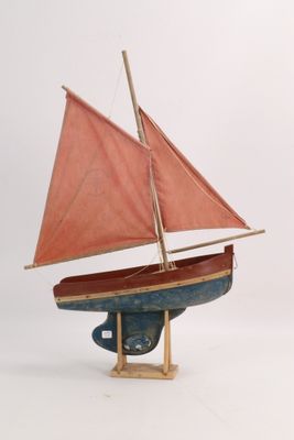 a small wooden boat with a red sail on a stand