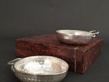 a silver bowl sitting next to a silver bowl on a wooden box