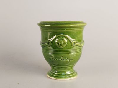 un vase vert orné d'un visage, posé sur une table