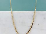 un gros plan d'un collier en or posé sur une surface en marbre