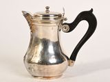 une cafetière ancienne en argent avec une poignée noire sur une surface blanche