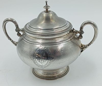 une théière en argent avec son couvercle, posée sur une table blanche
