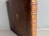 an old brown book sitting on top of a table next to a white wall