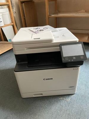 a printer that is sitting on the floor in front of a shelf