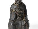 une vieille statue représentant un homme assis sur une chaise, coiffé d'un chapeau