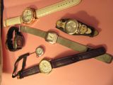 plusieurs montres différentes posées sur un fond rose, à côté d'un téléphone portable