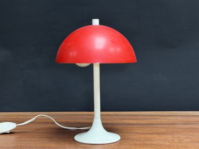 a red table lamp on a wooden table next to a computer mouse