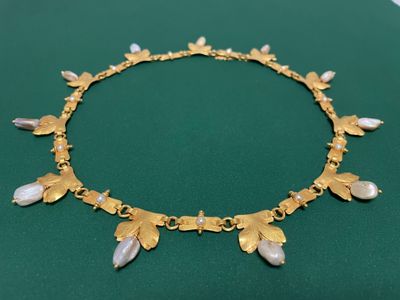 un gros plan d'un collier en or orné de perles, posé sur une surface verte