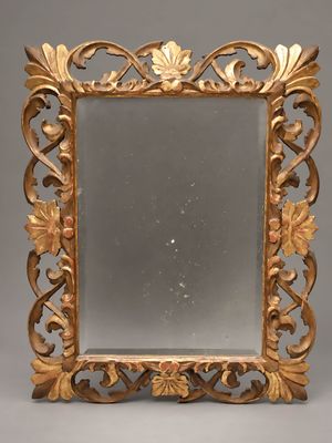 un miroir au cadre doré richement décoré, orné de feuilles et de volutes sur fond gris