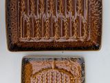 two brown ceramic trays with decorative designs on them on a white surface