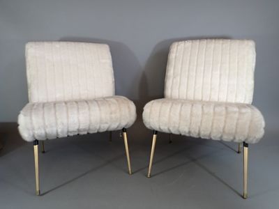 two white chairs with gold legs in a room with a gray wall