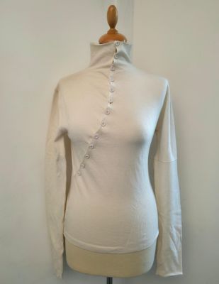 La chemise est blanche et comporte des boutons au niveau du col.