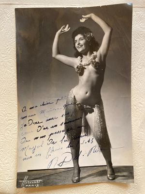 an old photo of a woman in a hula skirt holding a piece of paper