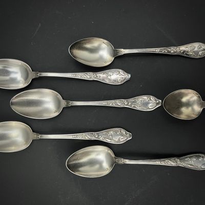 six cuillères en argent sont alignées sur une surface noire