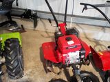 a small red tractor and a small red tiller in a garage