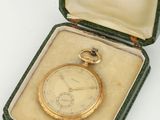 une montre de poche en or dans un écrin posé sur une surface blanche
