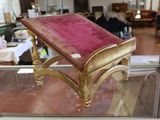 un banc doré sur lequel est posé un coussin rose