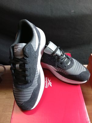 des chaussures de course grises et blanches posées sur une boîte rouge, elle-même posée sur une table en bois