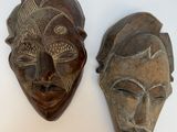 deux masques en bois posés sur une surface blanche, sur fond blanc