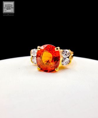 a close up of a ring with an orange stone surrounded by diamonds
